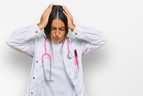Beautiful hispanic woman wearing doctor uniform and stethoscope suffering from headache desperate and stressed because pain and migraine. hands on head.  - Foto, Bild