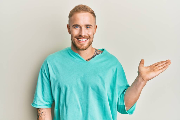 Young caucasian man wearing casual clothes smiling cheerful presenting and pointing with palm of hand looking at the camera.  - Foto, Imagen