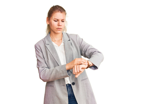 Young beautiful blonde woman wearing elegant jacket checking the time on wrist watch, relaxed and confident  - Photo, Image