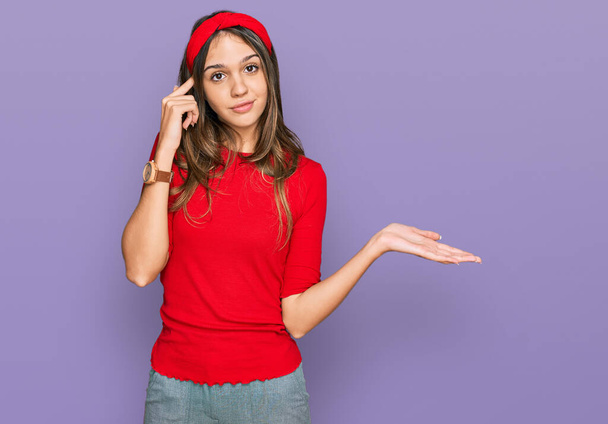 Young brunette woman wearing casual clothes confused and annoyed with open palm showing copy space and pointing finger to forehead. think about it.  - Photo, image
