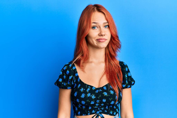 Young beautiful redhead woman wearing casual clothes over blue background looking sleepy and tired, exhausted for fatigue and hangover, lazy eyes in the morning.  - Photo, Image