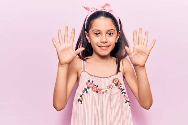 Kaunis lapsi tyttö päällään rento vaatteita näy ja osoittaa sormilla numero kymmenen hymyillen luottavainen ja onnellinen.  - Valokuva, kuva