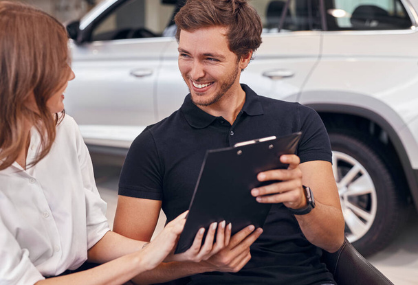 Happy couple reading contract in car dealership - Photo, Image