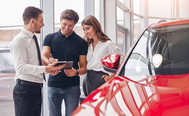 Delighted couple and manager signing papers in car dealership - Foto, immagini