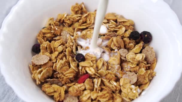 Slow motion milk is poured into a white cup with muesli and pieces of fruit and berries. Close up. Healthy breakfast concept - Footage, Video