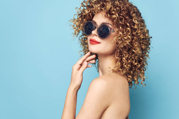 Pretty woman Curly hair dark glasses red lips smile blue background bare shoulders  - Photo, Image