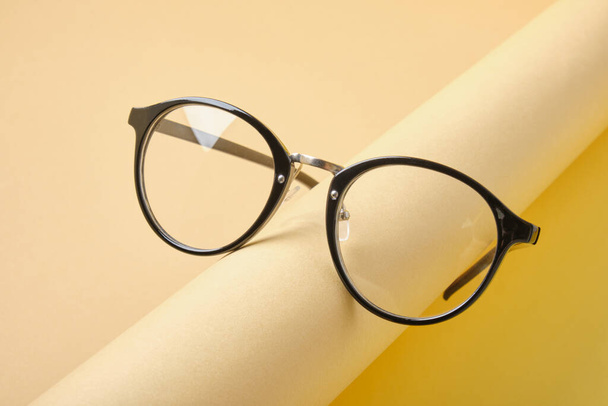 szemüveg egy tekercs bézs papír, geometriai háttér, trend színek, sárga háttér - Fotó, kép