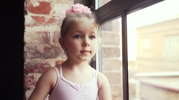 Schöne süße kleine Mädchen blonde Mädchen mit einer rosa Schleife auf dem Kopf geht am Fenster entlang. Zeitlupe - Filmmaterial, Video