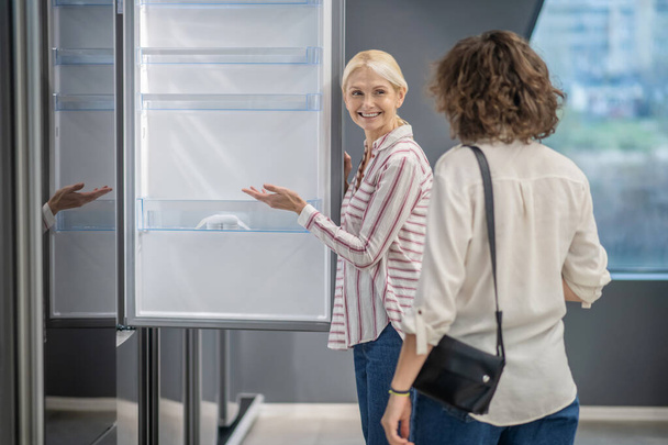 Sales assistant in striped shirt showing a new fridge to the female customer - Photo, Image