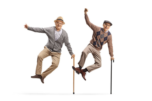 Beyaz arka planda zevkle zıplayan bastonlu iki heyecanlı yaşlı adamın tam boy portresi. - Fotoğraf, Görsel