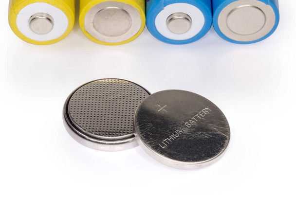 Twee lithium knoopbatterijen tegen de batterijen andere type op een licht oppervlak, close-up in selectieve focus - Foto, afbeelding