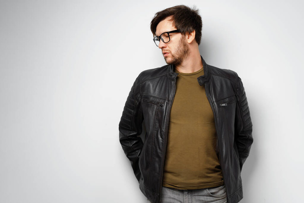 Portrait of a young man in glasses wearing black leather jacket on grey background - 写真・画像