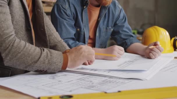 Midsectieopname van twee ingenieurs met potloden en architectuurplan in samenwerking op de bouwplaats - Video