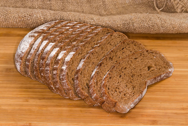 Κόψαμε το μισό καρβέλι ψωμί ψημένο με σιτάρι και αλεύρι σίκαλης σε ξύλινη επιφάνεια - Φωτογραφία, εικόνα