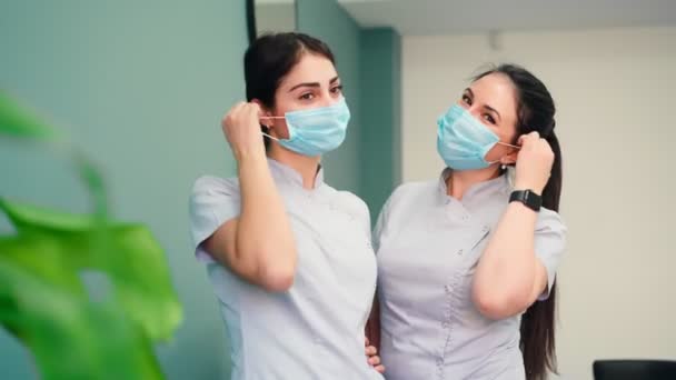 Dos enfermeras se quitan las máscaras médicas de la cara y sonríen para la cámara - Metraje, vídeo