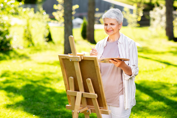 senior woman with easel painting outdoors - Φωτογραφία, εικόνα