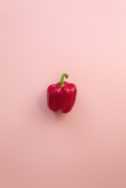 The vertical photo shows a juicy and healthy vegetable. This is red bell pepper. It's raw and whole. The vegetable lies in the Center on a pink background - Φωτογραφία, εικόνα