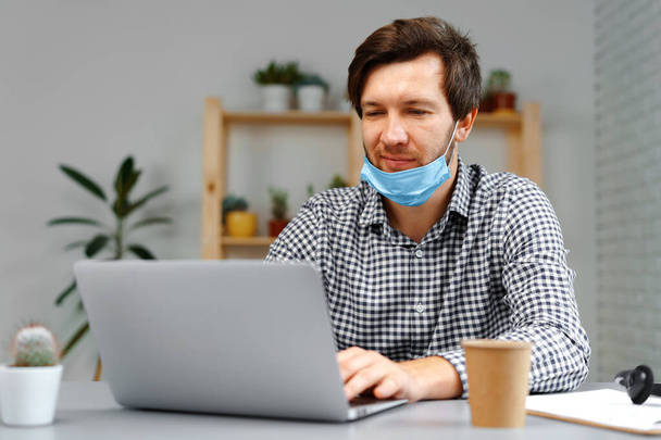 Man working on laptop at home and wearing medical mask - Foto, Bild