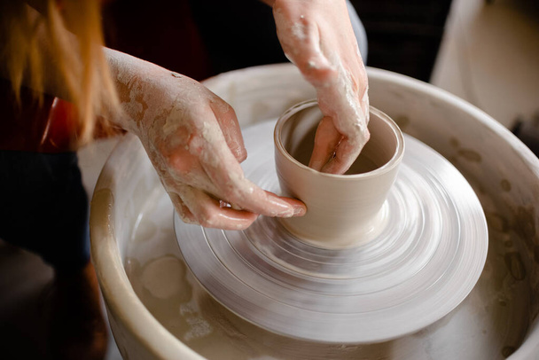 Vrouwelijke handen die een pottenbakkertje op een pottenbakkerswiel maken. Handgemaakte en ambachtelijke concept. - Foto, afbeelding
