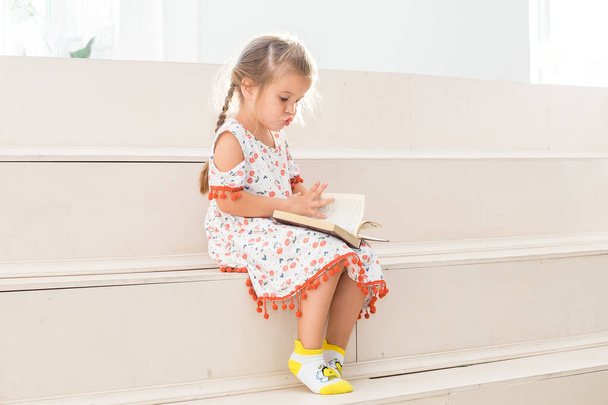 Little girl sitting on the steps and reading a big book. - Fotó, kép