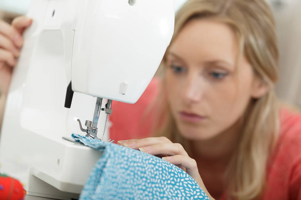 beautiful smiling tailor enjoying work on sewing machine - Фото, изображение