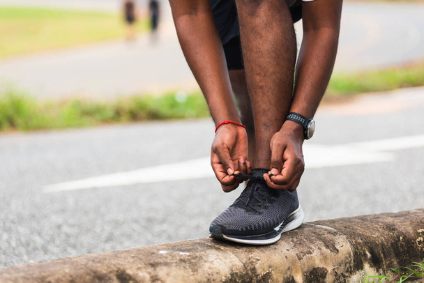 Закрийте азійського спортсмена Чорний чоловік носить годинник стоп на стежці, намагаючись взуття для бігу, готуючись до бігу на вулиці, і бігати на вулиці парк охорони здоров'я, здорова концепція тренування - Фото, зображення