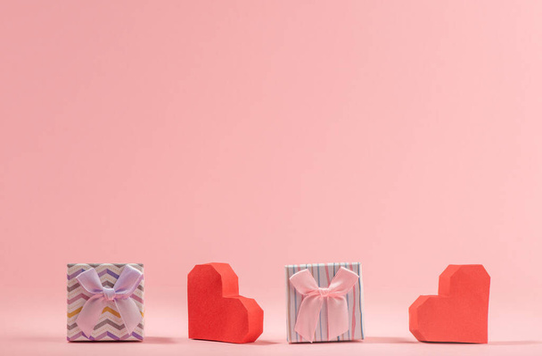 Gift boxes and red paper hearts on pink background - 写真・画像
