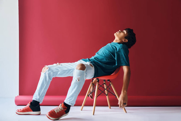 Portrait of tired young man sitting on chair in studio - Zdjęcie, obraz