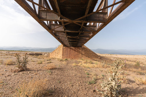 старый металлический мост на юге Испании, мало растительности, есть ветряные турбины и небо имеет облака - Фото, изображение