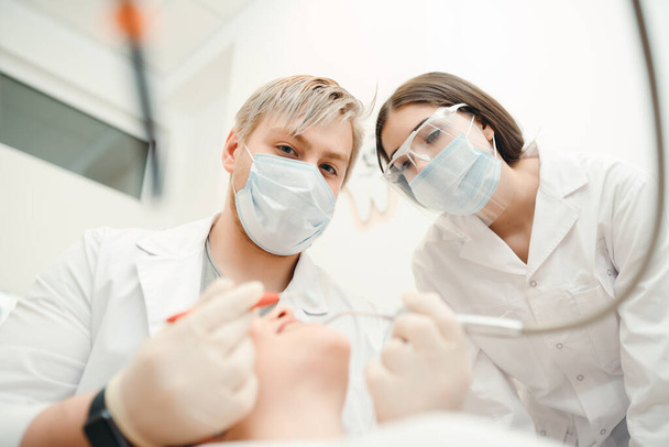 The doctor performs the dental treatment procedure for the client while the assistant looks at it - Fotografie, Obrázek