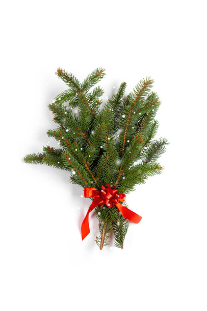 新鮮な若いトウヒの枝は白い縦の背景に赤いサテンリボンで花束。最小限のクリスマス廃棄物の概念。装飾的なクリスマスの休日の組成 - 写真・画像