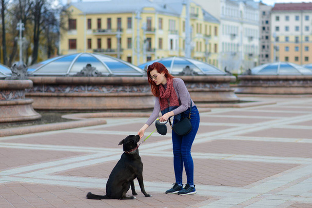 Beautiful happy young woman with cute black dog have fun on street. Concept about friendship between animals and people. - Foto, Imagem