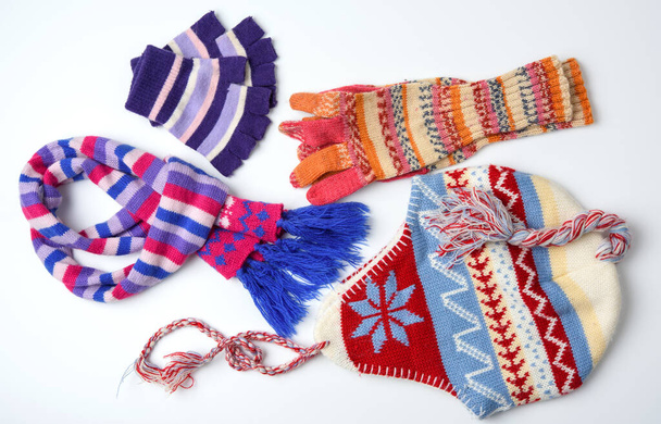 зимовий капелюх, рукавички та різнокольоровий в'язаний шарф на білому тлі, набір на білому тлі, вид зверху
 - Фото, зображення