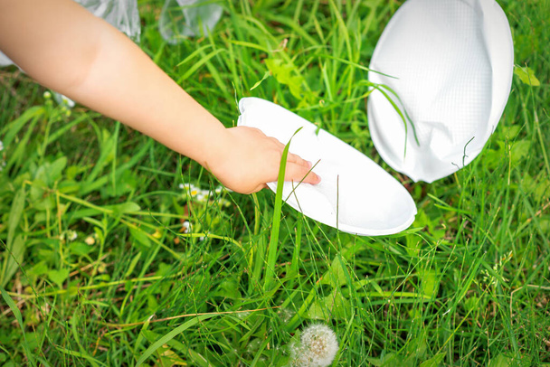 Kinderhand reinigt park van plastic gebruiksvoorwerpen in het gras in het park - Foto, afbeelding