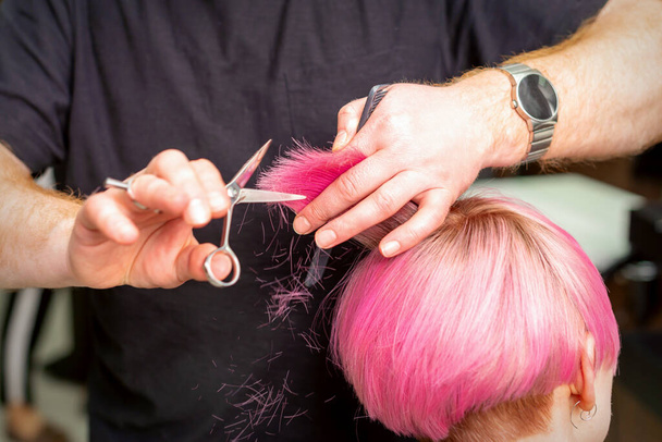 Крупный план парикмахера, стригущего короткие розовые волосы молодой женщины в парикмахерской - Фото, изображение