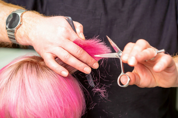 Gros plan du coiffeur coupant les cheveux roses courts de la jeune femme dans un salon de coiffure - Photo, image