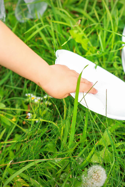 Kinderhand reinigt park van plastic gebruiksvoorwerpen in het gras in het park - Foto, afbeelding