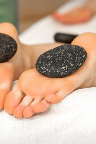 Massage-Steine, die auf Sohlen nackter Füße von Frauen im Wellness-Salon liegen - Foto, Bild