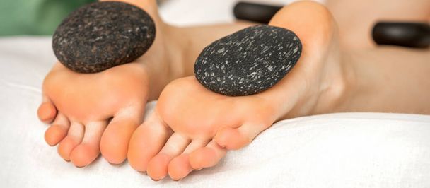 Kamienie do masażu leżące na podeszwach kobiecych gołych stóp w salonie spa - Zdjęcie, obraz