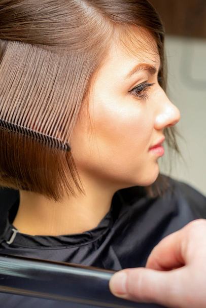 Close-up van een kapper rechttrekken kort bruin haar met haar ijzer in een kapsalon - Foto, afbeelding