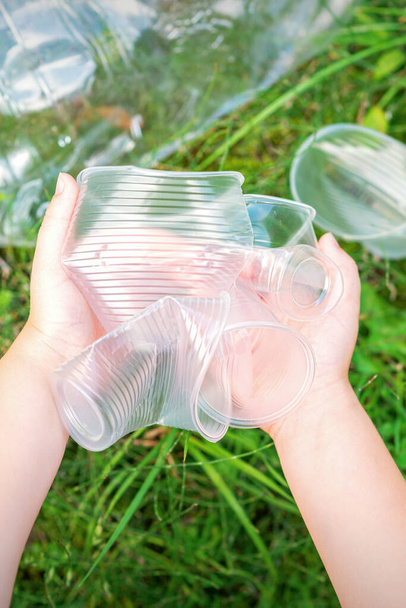 Детские руки очищают парк от использованной пластиковой посуды в траве - Фото, изображение
