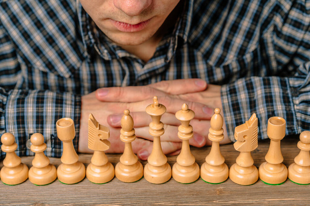 Чоловік у плетеній сорочці нахилився над низкою шахових фігур
 - Фото, зображення
