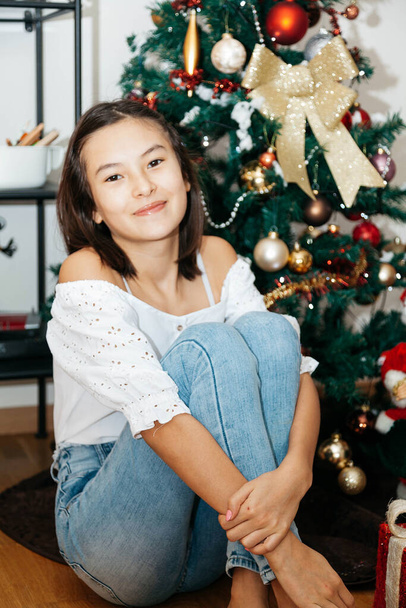 Beautiful teenage girl 12-year old sitting with Christmas presents under Christmas tree. Sitting on floor in room - Foto, Imagem