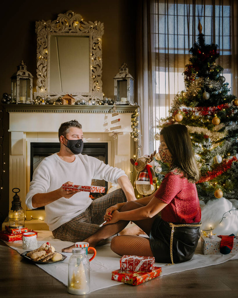 Boże Narodzenie para noszenie maski podczas nocy Bożego Narodzenia, zbliżenie portret szczęśliwy mieszane rasy para z prezentów świątecznych i noszenia masek medycznych w kwarantannie  - Zdjęcie, obraz