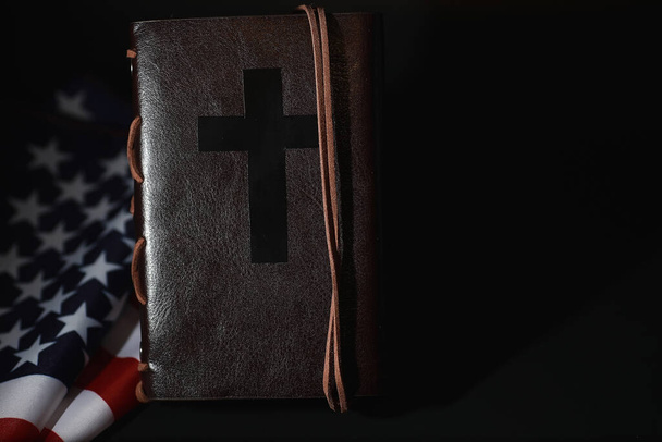 Американский флаг и священная книга Библии на зеркальном фоне. Символ Соединенных Штатов и религии. Библия и полосатый флаг на черном фоне. - Фото, изображение