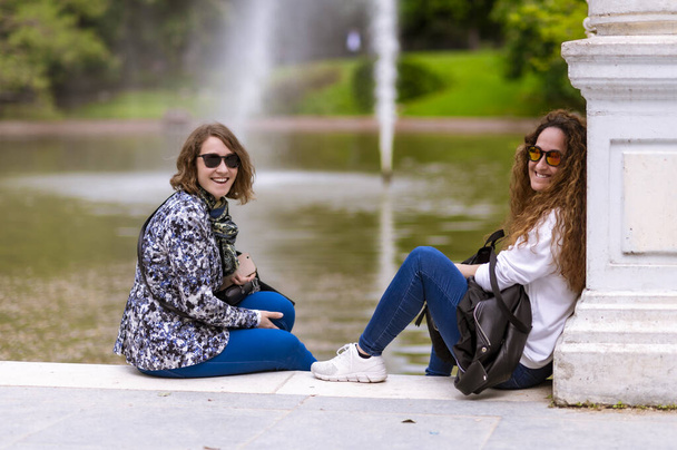 Говоря сидя на озере с фонтаном, они мать и дочь. - Фото, изображение
