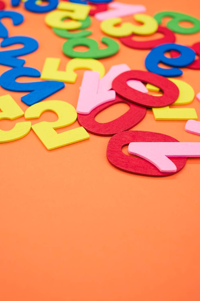 A closeup shot of the colorful wooden numbers scattered on an orange surface - space for text - 写真・画像