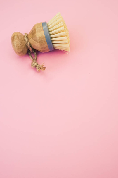 A closeup of a wooden round dishwashing brush on a pink surface - space for text - 写真・画像
