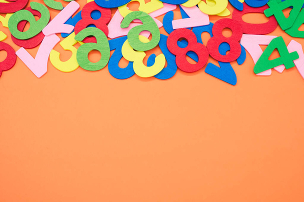 A closeup shot of the colorful wooden numbers scattered on an orange surface - space for text - Foto, Imagem