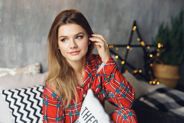 Close up of girl wears festive pajamas and take pillow in hands at home. Happy woman in red night-wear on bed - Foto, afbeelding
